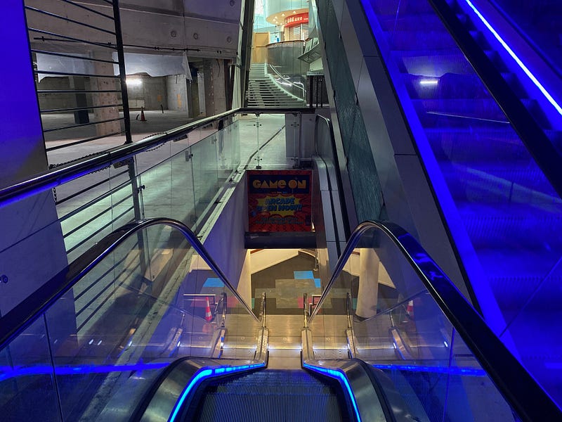 A neon escalator leading to a fading arcade.